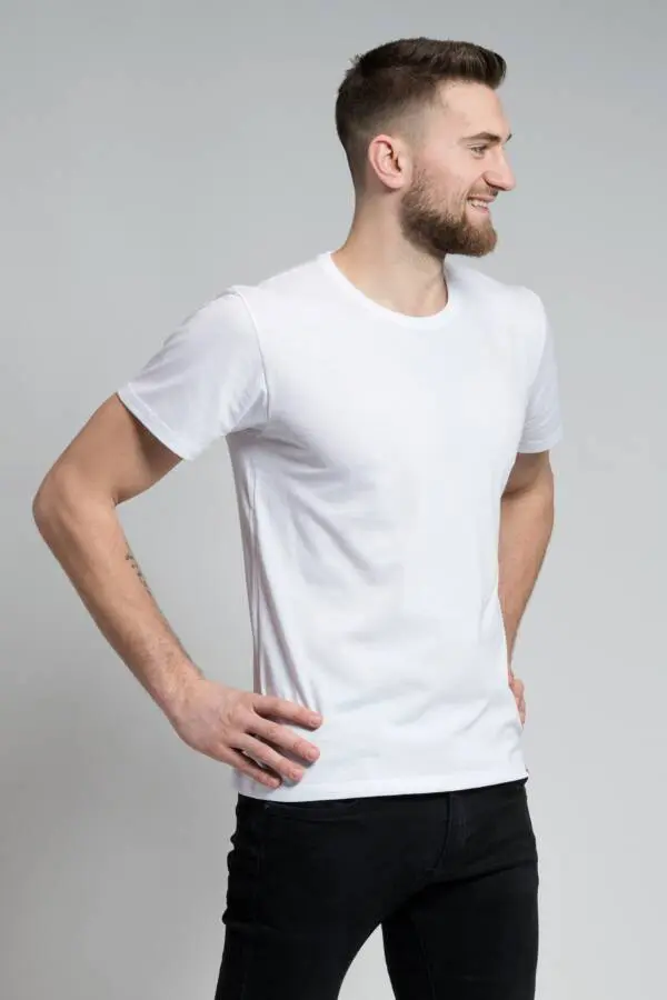 Model v bílém tričku a černých kalhotách pózuje s úsměvem pro e-shop MK Tailor.